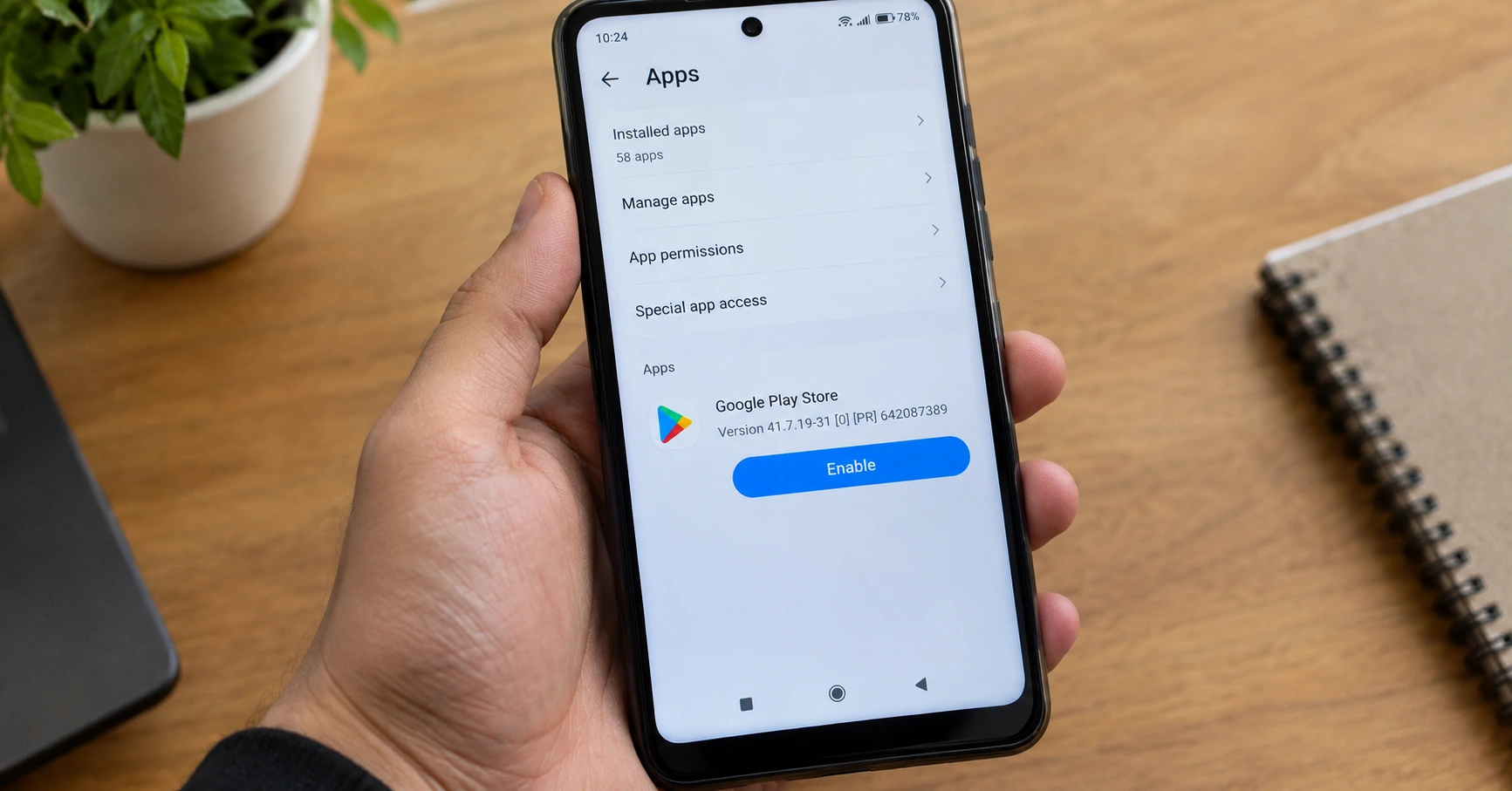 Hand holding Android phone showing Google Play Store in Settings app with Enable button visible